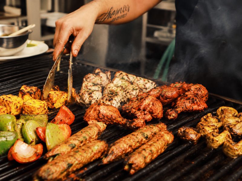 Chef turning paneer tikka, seekh kebabs and tandoori chicken on a live grill
